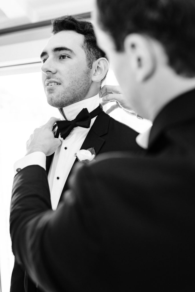 Best man helping groom get ready by adjusting bowtie.