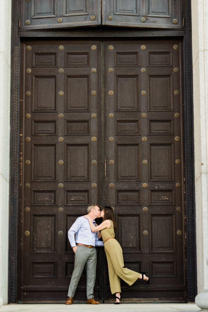 Couple kissing in front of tall door.