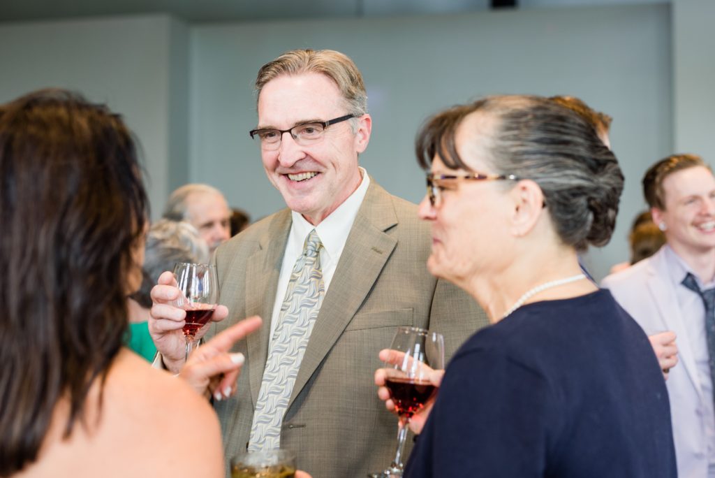 Gentleman smiling while holding a glass of wine and talking to others.