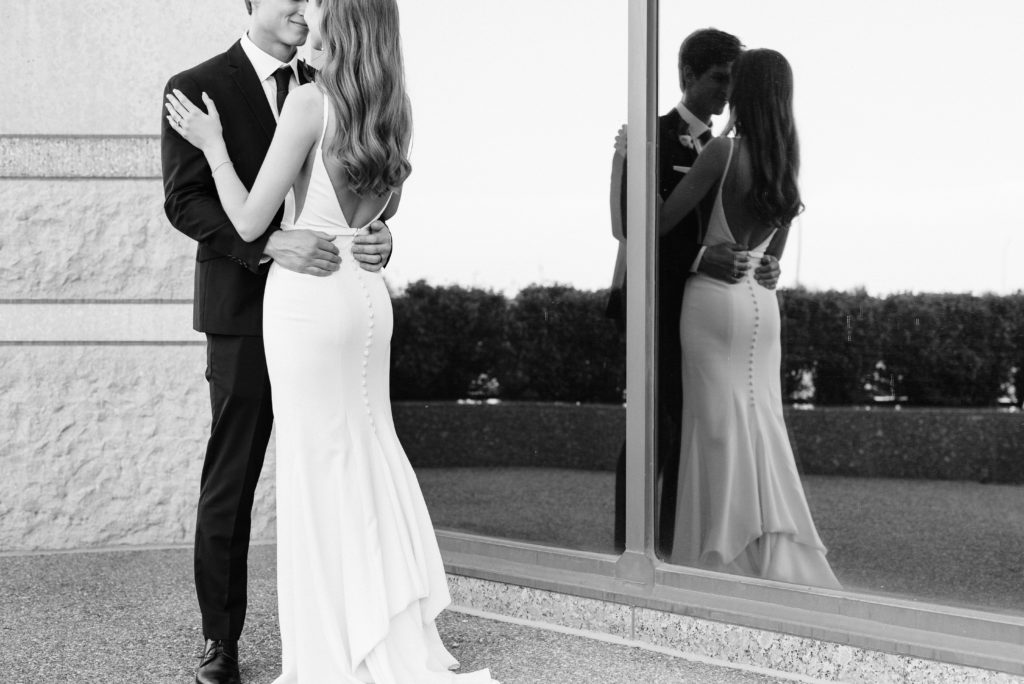 The bride and groom holding each other with their reflection in the window.
