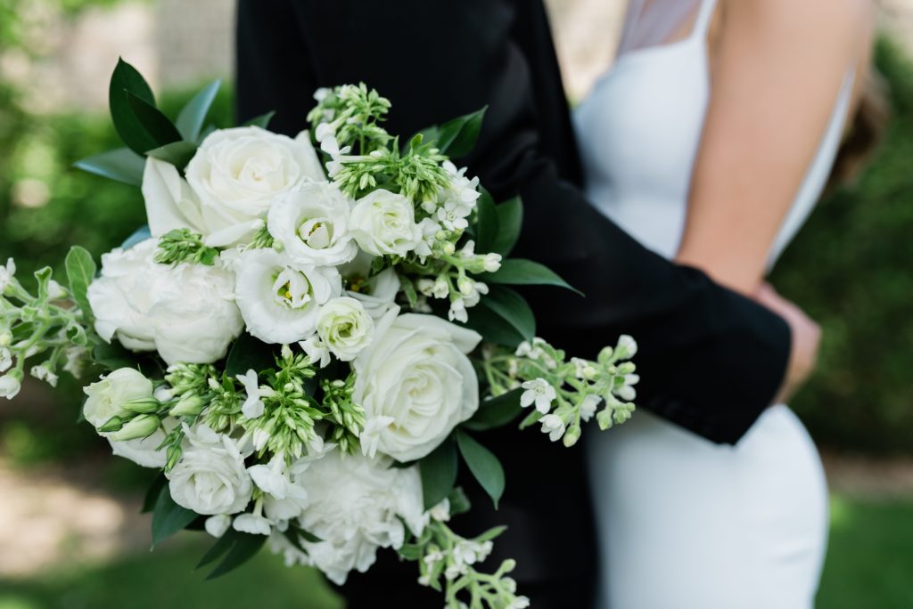 Detail of the bride and groom holding each other with a bouquet of flowers.