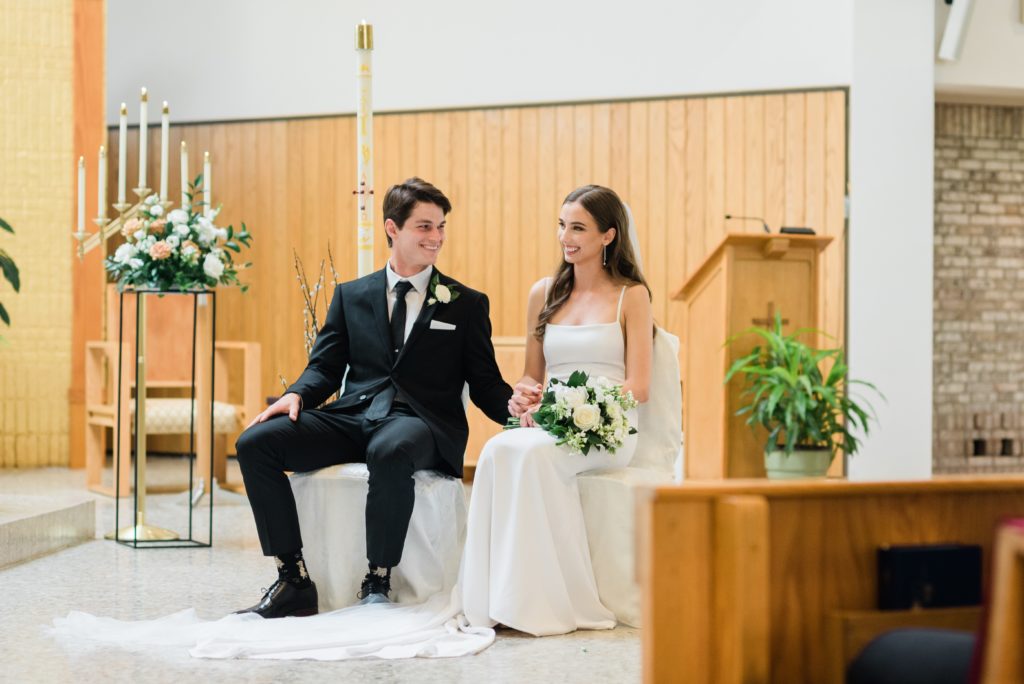 The bride and groom laughing while sitting at the altar during a catholic ceremony. 