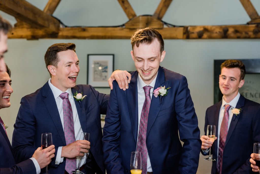 The groom and groomsmen laughing while looking down at a poker table.