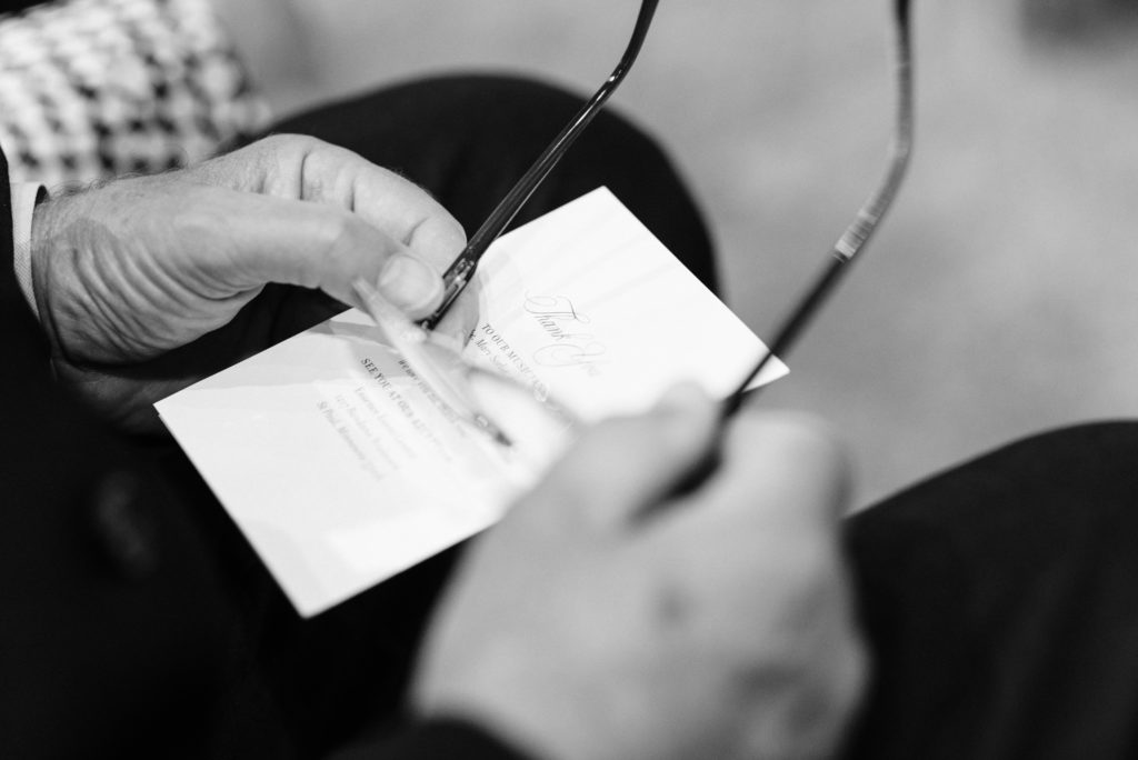A wedding guest holding his glasses and thank you card.