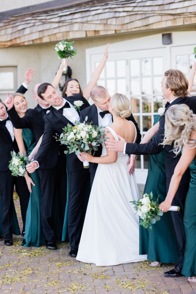 Bride and groom kiss with bridal party cheering. 
