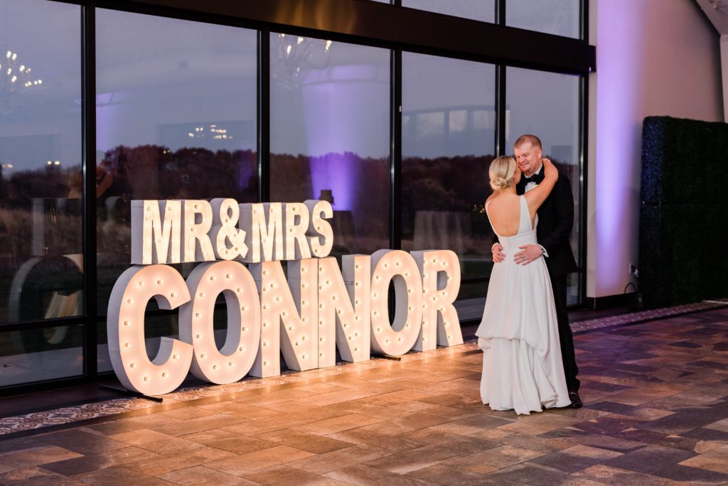 Bride and groom share their fist dance with their last name is in large letters behind them.
