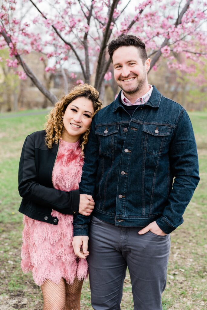 Couple smiling in front of pink blossoms. 