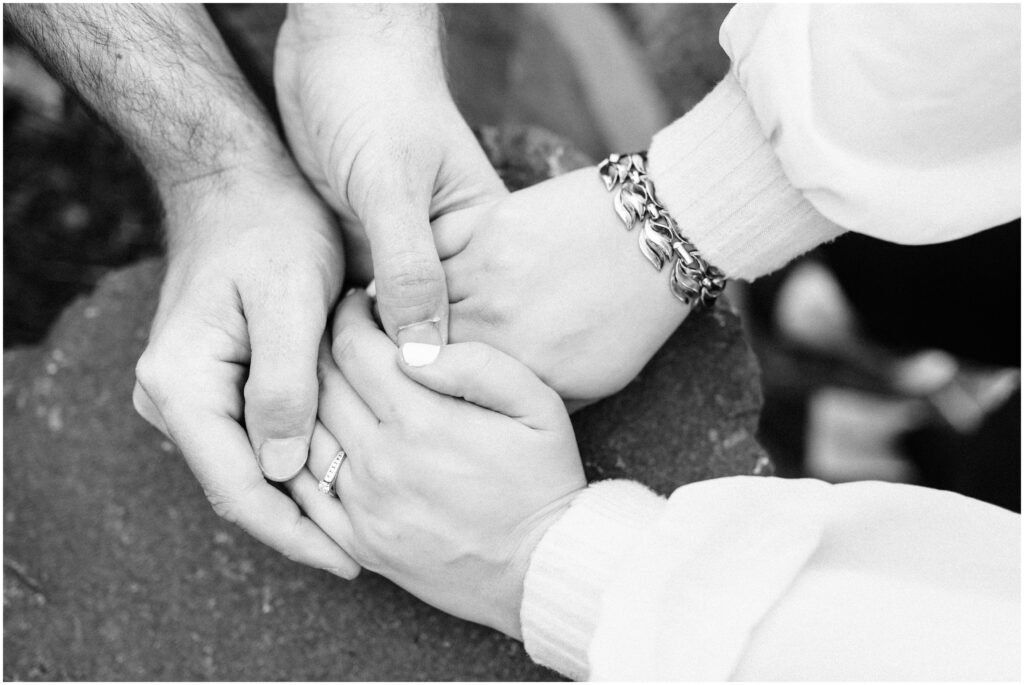 Black and white image of hands holding with engagement ring showing.