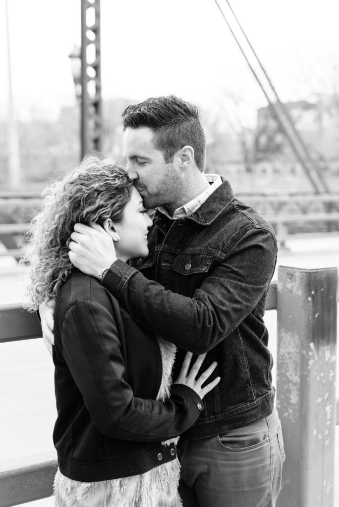 Boyfriend kissing girlfriend's forehead on a bridge.