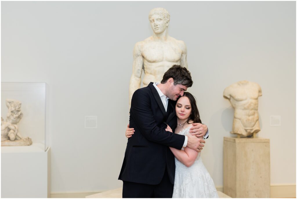 Groom hugs his bride in an art gallery.