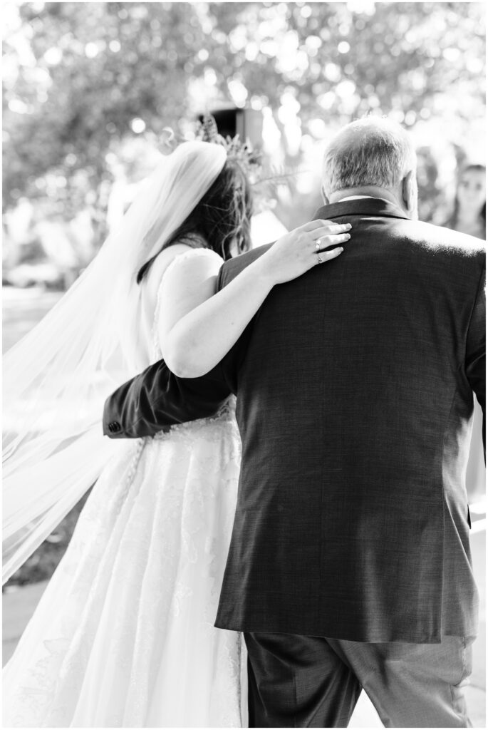 Bride holding onto her dad's shoulder while walking down the isle. 