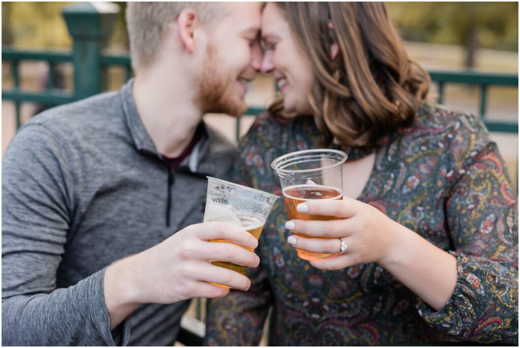 Girl and boy cuddle while holding beer.