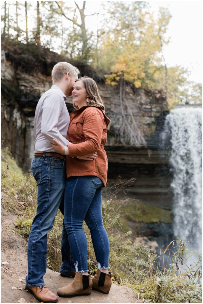 A couple is hugging in front of Minnehaha Falls.