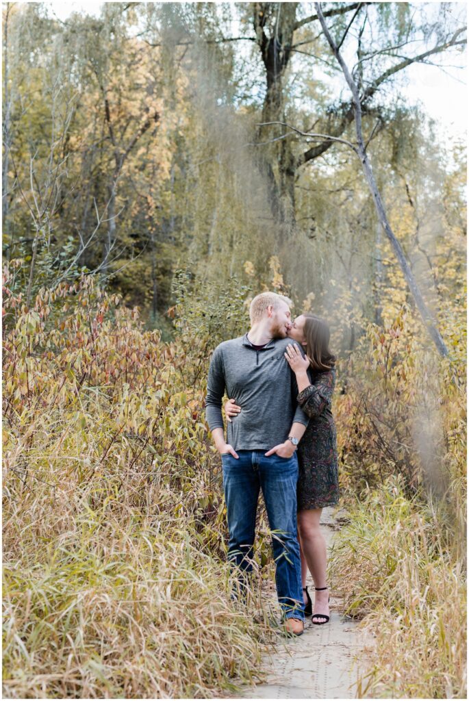 An engaged couple kiss on one of the trails of at Minnehaha Falls Regional Park.