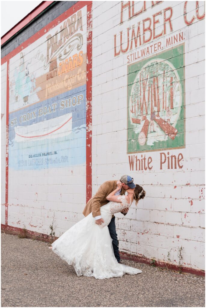 The bride and groom kissing in front of a mural downtown Stillwater, MN. 