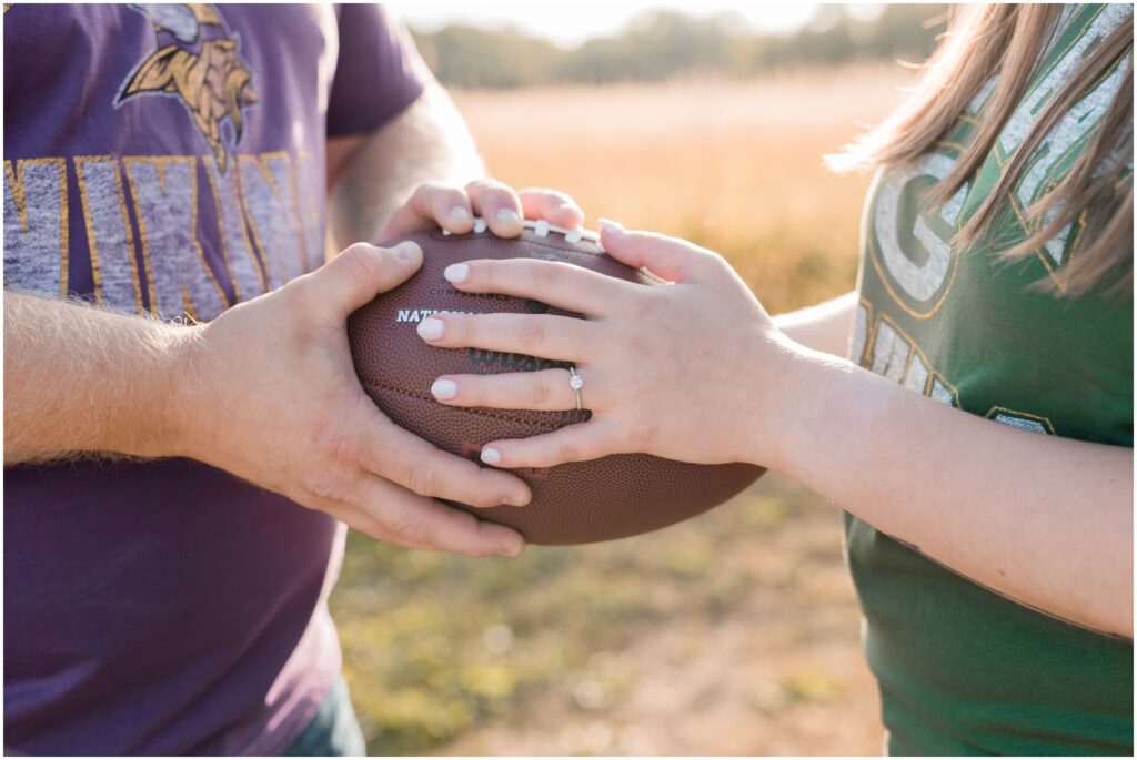 An engaged couple's hands holding a football while wearing football shirts. 