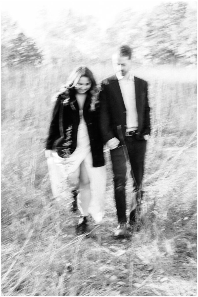 A black and white blurry photo of an engaged couple walking in a field.