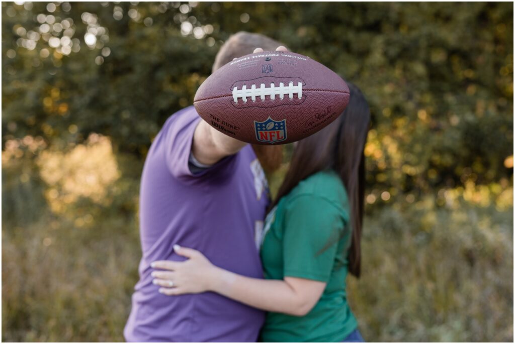 A couple kissing behind a football at Otsego County Park.