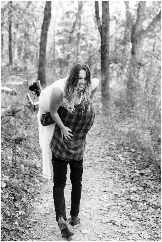 Boyfriend is holding his girlfriend over his should as he walks away on a trail .