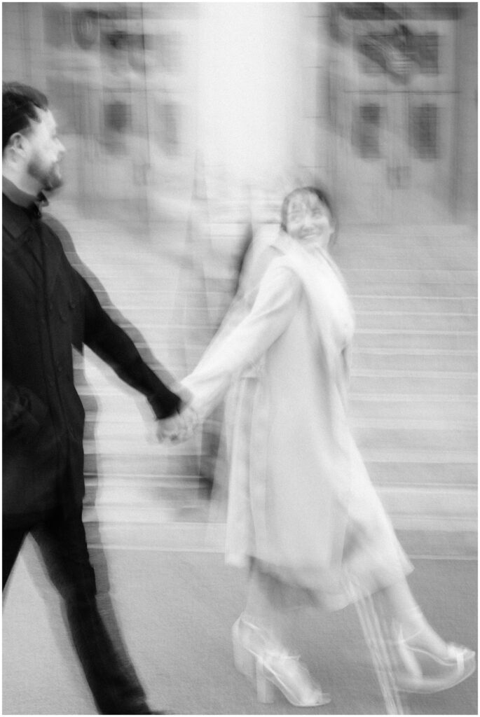 A blurry photo of a couple walking as the girlfriend leads her boyfriend. 