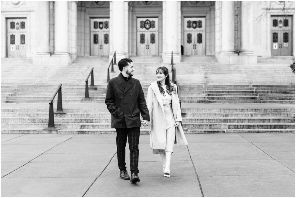 An engaged couple walk in front of the steps of the Minneapolis Basilica. 