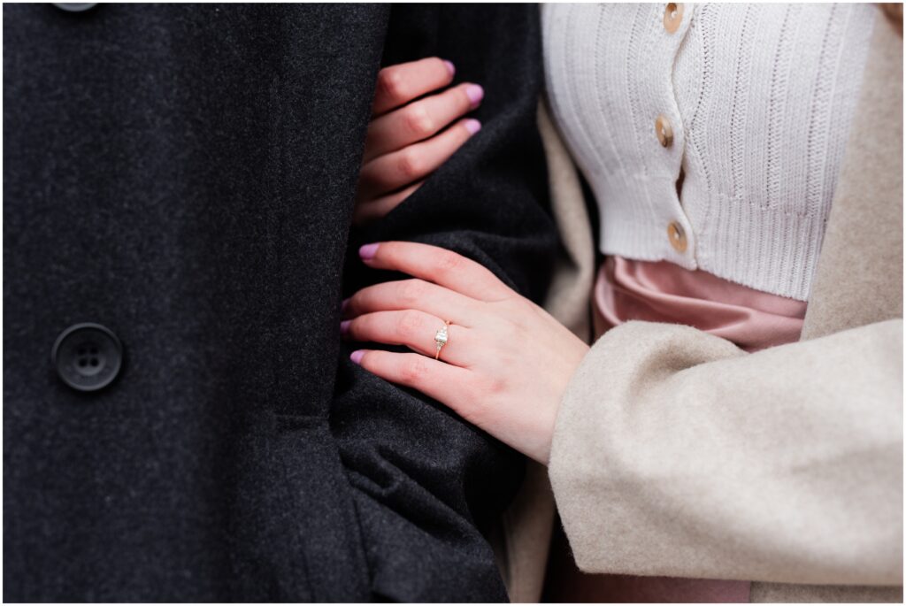 An engaged couple holding arms with the engagement ring on her finger. 